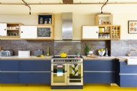 Cuisine rétro moderne avec briques apparentes, sol en caoutchouc jaune, armoires bleues, contreplaqué, éclairage de tuyaux en cuivre