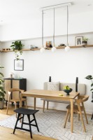 Salle à manger contemporaine minimaliste scandinave avec table en bois, pendentifs, meubles de couleur noir et chêne, étagères ouvertes et banquette