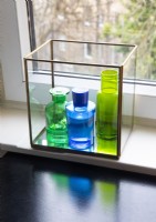 Verrerie bleue et verte dans une boîte en verre sur le rebord de la fenêtre - détail