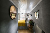 Chambre contemporaine sur canal, étroite, bateau fluvial avec murs gris foncé, parquet, plafond peint en blanc, miroir rond, hublot et jeté jaune.