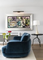 Salon avec canapé en tissu courbé bleu, tables d'appoint rondes en métal avec lampe de table et peinture, art mural.