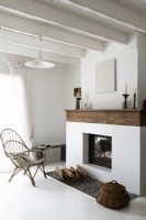 Salon peint en blanc avec chaise en osier à côté de la cheminée