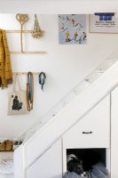 Escalier peint en blanc avec rangement intégré et lit pour chien. Des œuvres d'art et des crochets sont accrochés au mur.