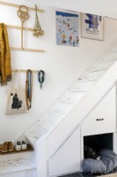 Escalier peint en blanc avec rangement intégré et lit pour chien. Des œuvres d'art et des crochets sont accrochés au mur.