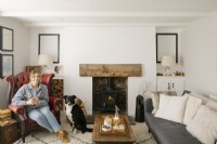 Kati Scalet assise dans son salon décloisonné contemporain dans un cottage de Cornouailles. Doté d'un poêle à bois et d'un fauteuil à oreilles en cuir rouge.
