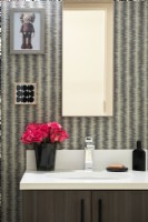 Lavabo de la salle de bain avec miroir et œuvres d'art sur les murs et vase de roses exposé.