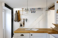 Au premier plan se trouve une cuisine contemporaine en forme de L avec des carreaux de métro blancs et une surface de travail en bois et des armoires grises.
