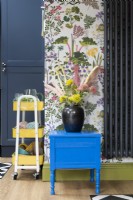 Table d'armoire peinte recyclée contre papier peint floral avec chariot de rangement jaune
