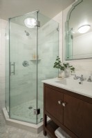Salle de bain moderne avec douche vitrée et meuble lavabo blanc et marron.