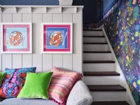 Œuvres d'art océaniques sur un mur lambrissé blanc au-dessus de coussins colorés et à côté d'un petit escalier blanc