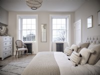 Chambre neutre avec un lit, une chaise rembourrée, des tiroirs et des fenêtres symétriques