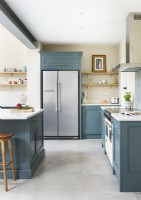 Cuisine classique moderne avec placards bleus, îlot, étagères ouvertes, carrelage au sol en béton et réfrigérateur intégré.