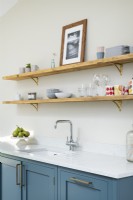 Étagères en bois ouvertes dans une cuisine classique moderne avec supports en laiton, unités bleues, comptoir blanc et robinets.