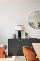 Buffet gris foncé moderne avec table d'appoint orange, lampe de table en céramique noire et miroir rond.