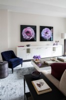 Salon moderne avec une longue crédence blanche décorée de photographies de fleurs au mur.