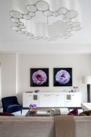 Salon moderne avec une longue crédence blanche décorée de photographies de fleurs sur le mur et un lustre unique.