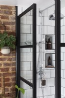 Douche avec portes de style crittall noires, tuiles carrées blanches et pomme de douche chromée.