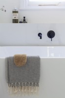 Détail d'une serviette de hammam sur une baignoire contemporaine autoportante. Robinets noirs.