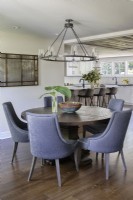 Table à manger ronde en bois et chaises rembourrées dans une salle à manger et une cuisine modernes à aire ouverte.