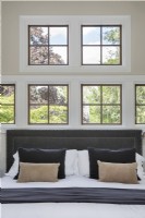 Gros plan sur un lit placé devant plusieurs fenêtres à carreaux avec vue sur le jardin.