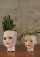 Détail de deux têtes de poupées utilisées comme pots de fleurs.