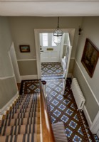 Une vue du hall d'entrée vu du premier étage, montrant un sol carrelé décoratif et un coureur rayé sur les escaliers.