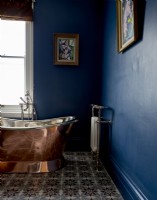 Détail de la baignoire sur pieds de couleur cuivre dans une salle de bains peinte en bleu avec peinture sur les murs.