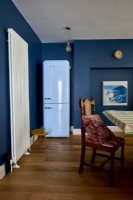 Détail d'une salle à manger montrant un réfrigérateur bleu et un radiateur mural vertical.
