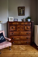 Commode antique dans une chambre à coucher à côté d'une chaise antique recouverte de tissu design William Morris.