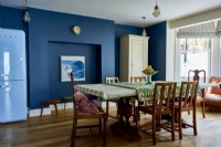 Une salle à manger ouverte, avec une table et des chaises du milieu du siècle, bébé de murs bleu foncé.