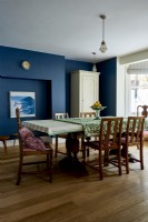 Salle à manger avec des murs peints en bleu foncé et une table et des chaises vintage et anciennes.