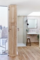 Salle de bain attenante ouverte avec douche et lavabo, plancher en bois et puits de lumière et vue sur les toits
