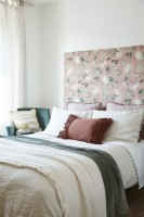 Détail de lit double avec tête de lit en tissu à motifs d'oiseaux et de fleurs et plaids, coussins, oreillers et fauteuil