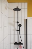 Détail de la salle de bain avec robinetterie de douche noire, carrelage blanc et mur peint en jaune.