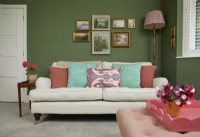 Salon avec un canapé crème, des peintures à l'huile vintage et un mur peint en vert.