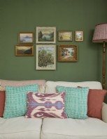 Détail du salon avec un canapé crème, des peintures à l'huile vintage et un mur peint en vert.