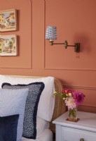 Détail de la chambre avec panneaux en terre cuite, coussins bleus texturés et luminaires muraux vintage.