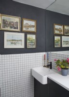 Détail de la salle de bain avec carreaux blancs carrés, murs gris et peintures à l'huile vintage.