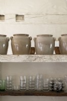 Détail de grands pots en céramique et verrerie sur des étagères rustiques
