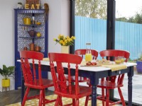 Détail de la salle à manger décloisonnée avec des chaises peintes en rouge et un tapis jaune à pois.