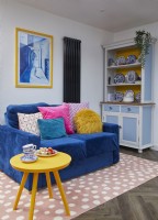 Coin salon décloisonné avec un canapé bleu, un placard à vaisselle et un tapis rose à pois.