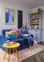 Femme lisant sur un canapé bleu avec une armoire à vaisselle et un tapis rose à pois.