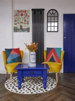 Coin salon avec des chaises jaunes, une table basse bleue et un tapis rond à pois.