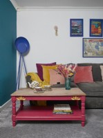 Salon avec un grand canapé gris, un mur peint en bleu sarcelle et une table basse rose.