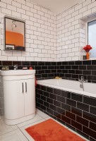 Salle de bain avec carrelage métro noir et blanc et accessoires orange.