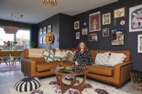 Salon avec un canapé en cuir marron, une table basse vintage, une galerie d'estampes encadrées et des murs peints en bleu foncé.