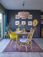 Salle à manger ouverte avec des chaises jaunes de style vintage, un tapis à motifs et des murs peints en bleu foncé.