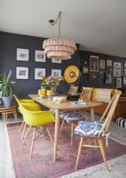 Salle à manger ouverte avec des chaises jaunes de style vintage, un tapis à motifs et des murs peints en bleu foncé.