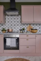 Détail de la cuisine avec four, armoires roses et carreaux à motifs.