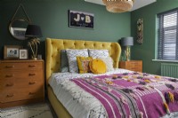 Chambre avec lit double jaune, tiroirs vintage en bois et murs peints en vert.